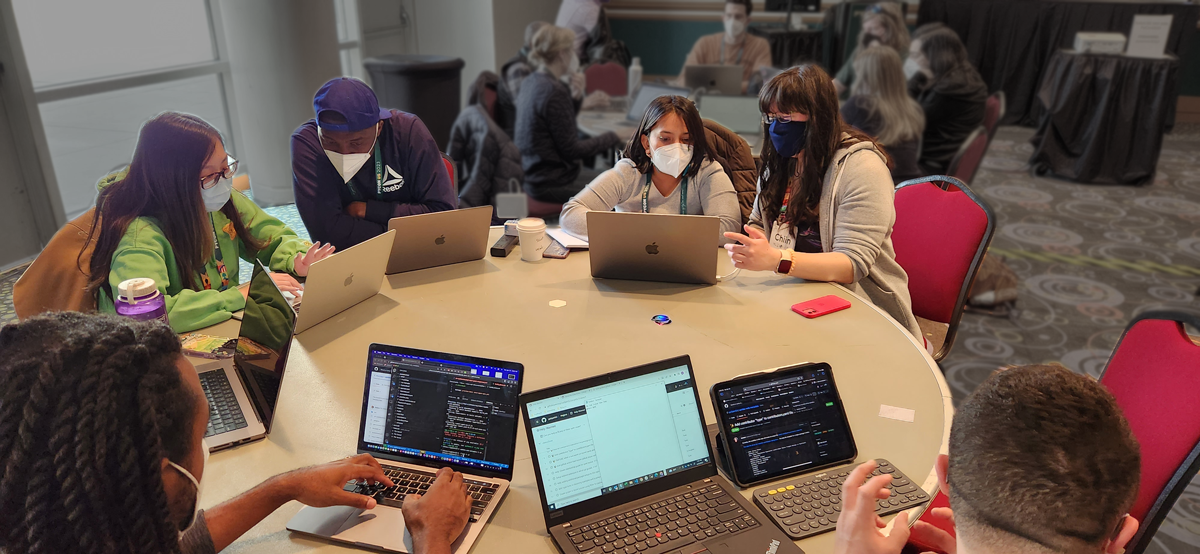Image showing people at laptops sitting around a round table wearing masks during our PyCon 2023 mentored sprint.
